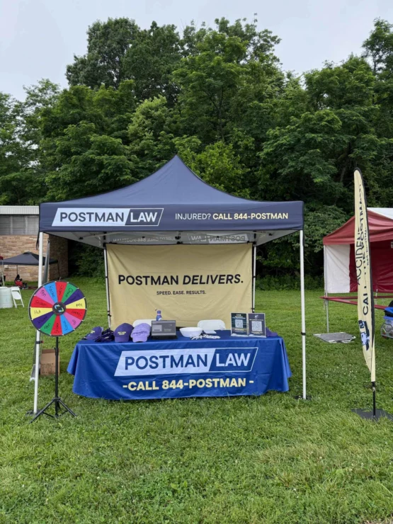 Postman Law outdoor event booth with branded canopy and table for legal services and community outreach.